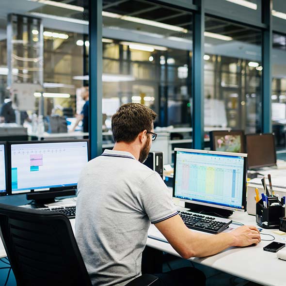 Man sitting in a desk using several computers